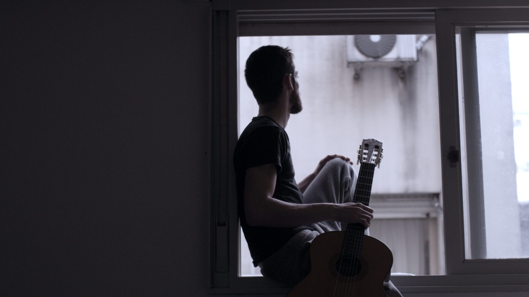 Un músico con su guitarra, a contraluz frente a una ventana